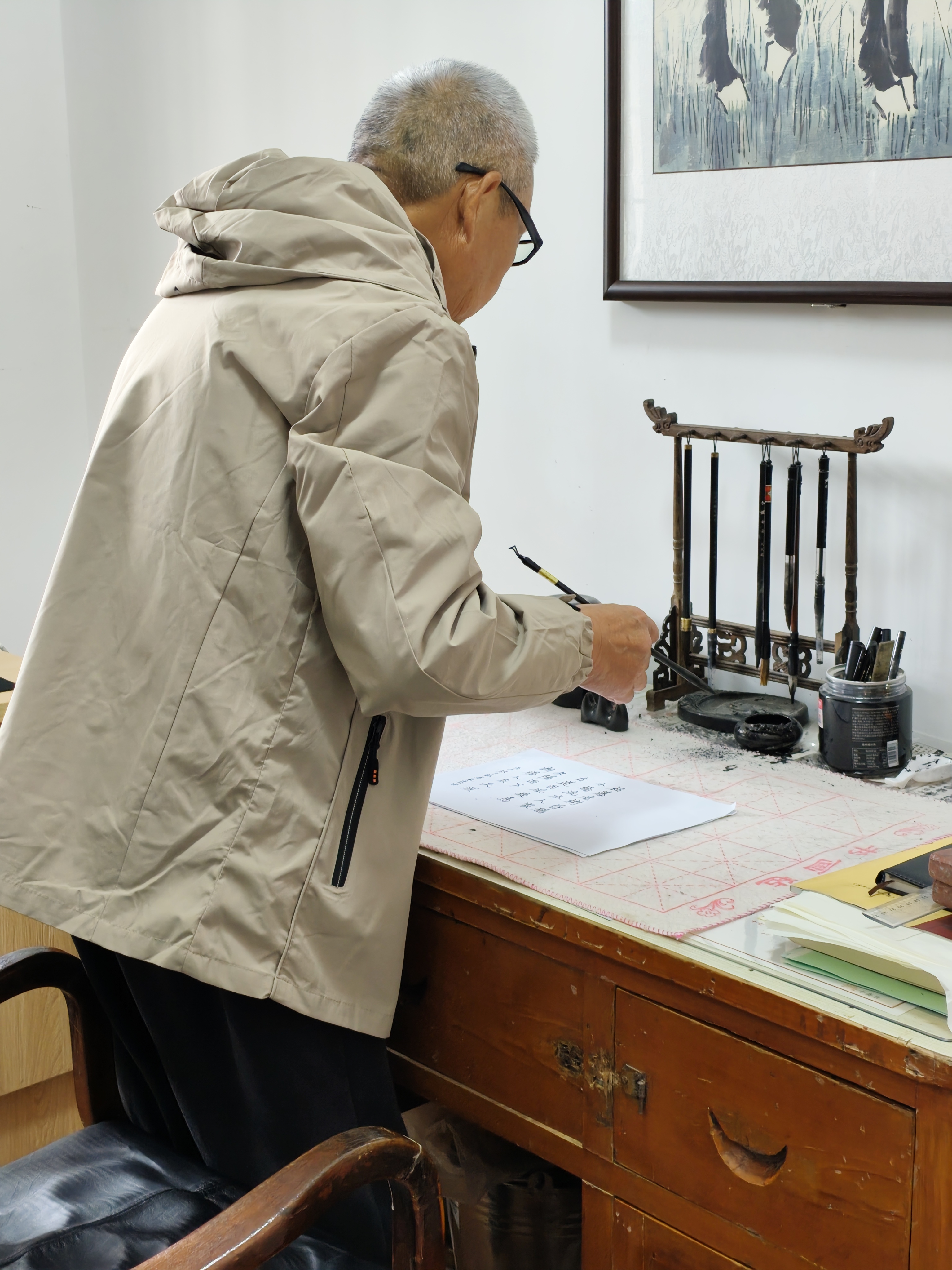 Qing Wu holding a brush above a handwritten page, beside an inkstone and hanging brushes